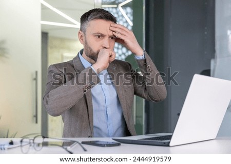 Worried businessman looking confused while working on a laptop in a contemporary office setting, displaying signs of stress or problem-solving.