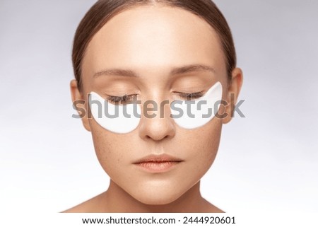 Closeup portrait of calm relaxed beautiful woman keeps eyes closed posing with under eye patches skin care. Indoor studio shot isolated over gray background.