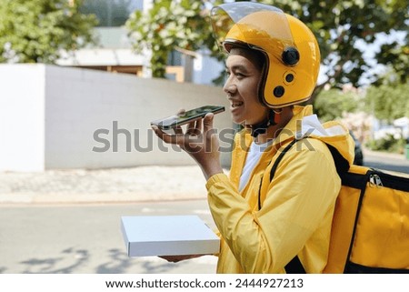 Smiling courier carrying pizza and recording voice message for customer