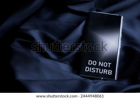 Modern smartphone with do not disturb inscription on the screen on a dark background of cosy fabric. The concept of rest and solitude of an introvert. Weekends and holidays. Photo. Close-up