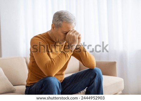 A contemplative senior wears a mustard sweater reflecting pensively with his head on his hand, suggesting deep thought or concern Royalty-Free Stock Photo #2444952903