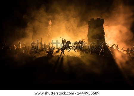 Medieval battle scene with cavalry and infantry. Silhouettes of figures as separate objects, fight between warriors on dark toned foggy background. Night scene. Selective focus Royalty-Free Stock Photo #2444955689