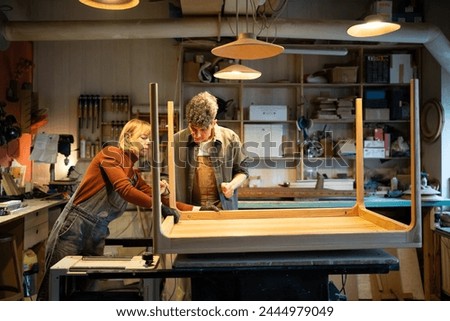 Carpentry workshop. Focused spouses woman man working in carpentry workshop assembling table, joining base and legs. Working together on an individual order. Furniture manufacturing, small business Royalty-Free Stock Photo #2444979049