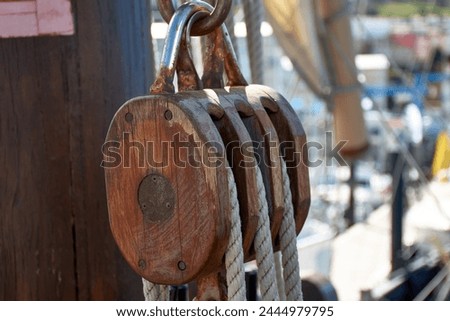 Pulley for sails and ropes made of wood on the replica of the Santa Maria caravel, with the sail and other ships in the harbor, soft and out of focus in the background Royalty-Free Stock Photo #2444979795