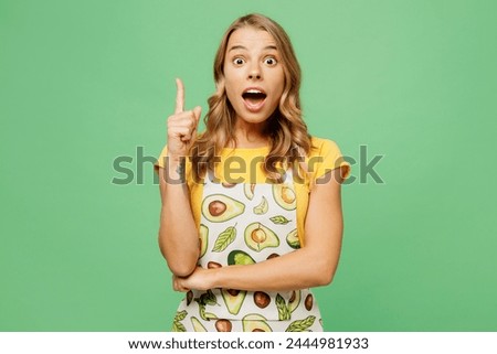 Young overjoyed housewife housekeeper chef cook baker woman wear apron yellow t-shirt point index finger up with new great idea isolated on plain pastel green background studio. Cooking food concept