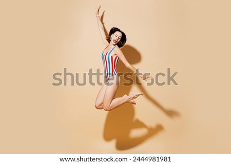 Full body side view young woman wear one-piece swimsuit straw hat near hotel pool jump high with outstretched hands arms isolated on plain beige background. Summer vacation sea rest sun tan concept