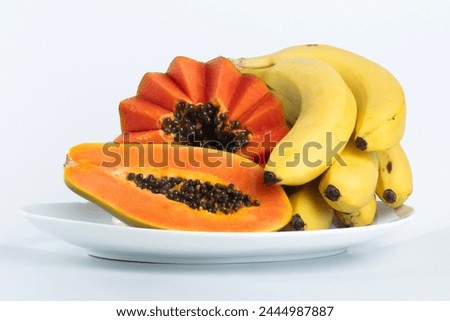 Tropical fruits, banana and papaya on a white porcelain plate photographed on white studio background