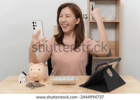 Asian woman smiling happily after looking at her mobile phone and seeing the benefits from playing the stock market. Stock market investment concept. Long-term savings.