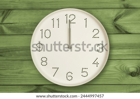Round white wall clock at 12 o'clock on green wood background. Concept of daily regime, lunch time, Daily Grind, Noon Break Royalty-Free Stock Photo #2444997457