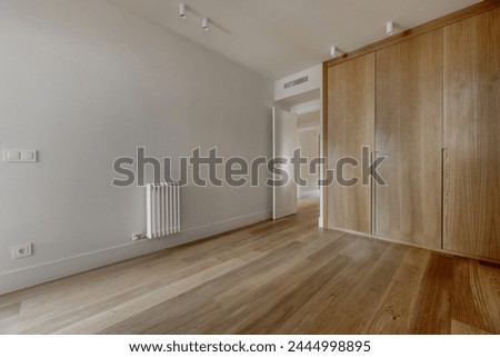 bedroom with built-in wardrobes with custom-made light oak doors, cast iron radiator, white painted walls, white shelves on the wall, white spotlights on the ceiling and light parquet flooring