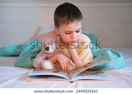 Thoughtful child hugs toy and reads his favorite book, looking at bright pictures. Child development concept.
