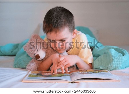 Thoughtful child hugs toy and reads his favorite book, looking at bright pictures. Child development concept.
