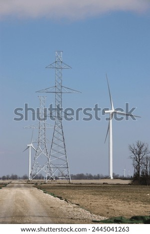 Newly erected hydro towers alongside wind turbines in open field Royalty-Free Stock Photo #2445041263