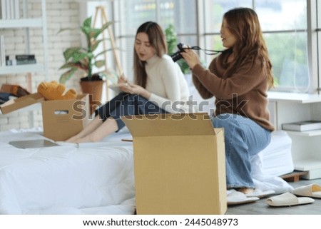 Two young Asian roommates prepared things in boxes, sat on their friend's bed, picked up a camera and took pictures before moving out of the rented apartment and moving to another place. Royalty-Free Stock Photo #2445048973