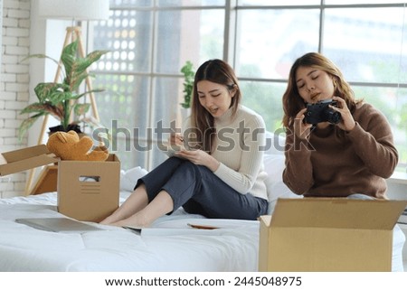 Two young Asian roommates prepared things in boxes, sat on their friend's bed, picked up a camera and took pictures before moving out of the rented apartment and moving to another place. Royalty-Free Stock Photo #2445048975
