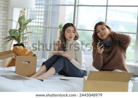Two young Asian roommates prepared things in boxes, sat on their friend's bed, picked up a camera and took pictures before moving out of the rented apartment and moving to another place. Royalty-Free Stock Photo #2445048979
