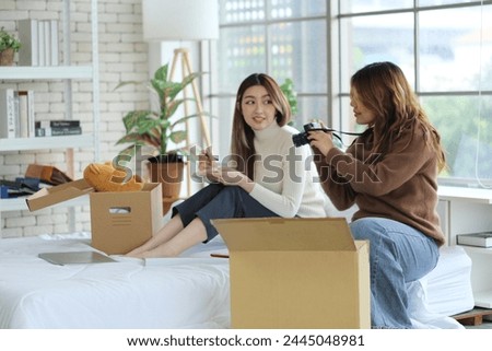 Two young Asian roommates prepared things in boxes, sat on their friend's bed, picked up a camera and took pictures before moving out of the rented apartment and moving to another place. Royalty-Free Stock Photo #2445048981
