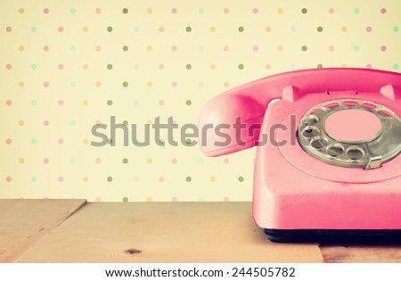 Retro pastel pink telephone on wooden table and abstract geometric pattern background
