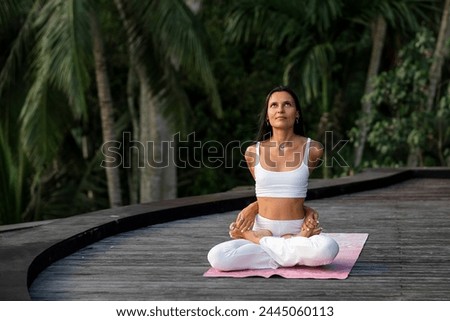 A beautiful young girl, of European appearance, brunette, doing yoga, wearing a white yoga suit.