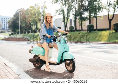 Young beautiful smiling hipster female in trendy clothes. Carefree woman driving retro motorbike on the street background. Positive model having fun, riding classic Italian scooter in Europe city Royalty-Free Stock Photo #2445060263