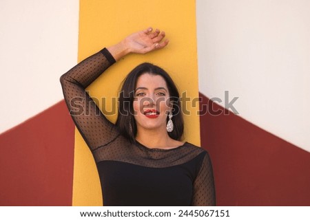 Young and beautiful brunette woman is dressed elegantly in a black dress with transparencies. The girl is leaning against the wall and is happy and smiling. Beauty and fashion concept