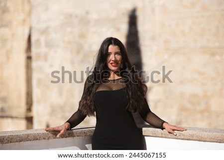 Beautiful young Spanish brunette woman with make-up and dressed in an elegant black dress. The woman is leaning on the railing. Beauty and fashion concept
