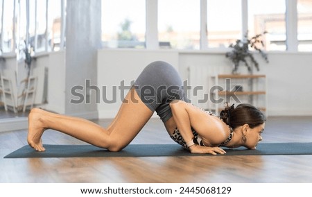 Athletic young woman enjoying daily yoga practice in serene studio environment, engaged in graceful challenging asana enhancing physical capabilities and inner balance..