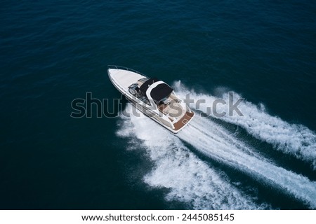 A large white motor boat moves quickly on dark blue water, top view. A white boat moves on the water, aerial view. Royalty-Free Stock Photo #2445085145