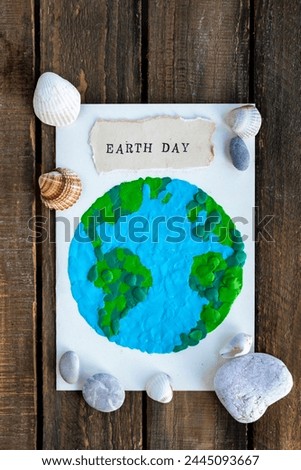 Children's craft for the Earth Day celebration. Little boy holding handmade simple postcard with a picture of our Planet made of plasticine. Concept of environment education for kids in kindergarten