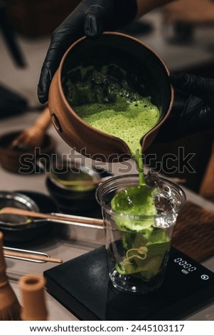 Matcha Japanese green tea making process. Female hands pouring matcha into a plastic glass. Traditional organic utensils. Royalty-Free Stock Photo #2445103117