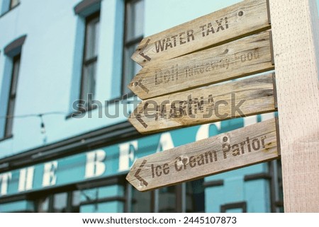 Beach and holiday concept image. A wooden signpost points to various seaside attractions. Tourism and information picture. Water taxi, Ice cream, Deli and Marina wording. Blue.