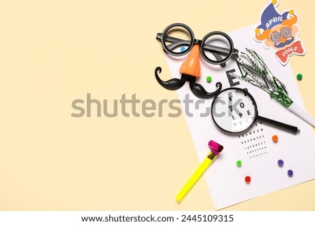 Eye test chart, magnifier and party decor for April Fools Day celebration on color background