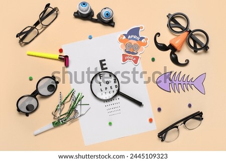 Eye test chart, eyeglasses, magnifier and party decor for April Fools Day celebration on color background
