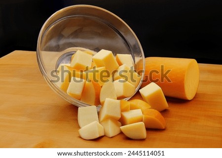 SMOKED PROVOLONE CHEESE IN PIECES FALLING FROM BOWL ON WOODEN BOARD WITH DARK BLACK BACKGROUND Royalty-Free Stock Photo #2445114051