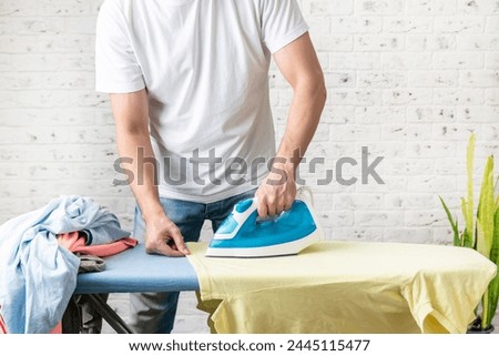 Close up photo of man holding flat iron and ironing clothes. Male household concept	