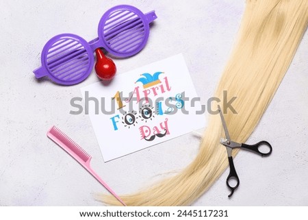 Card with text  APRIL FOOL'S DAY, hair strand and hairdresser's supplies on light background
