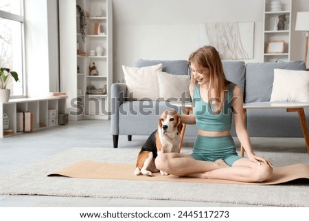 Sporty young woman with Beagle dog sitting on yoga mat at home Royalty-Free Stock Photo #2445117273