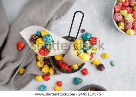 Paper cones with sweet colorful popcorn in deep fry basket on white table