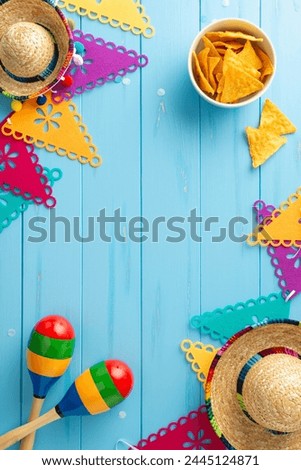 Vibrant Cinco de Mayo top view vertical display with sombreros and maracas. Bright flag garland, and spicy nacho on a blue wooden desk. Space available for text Royalty-Free Stock Photo #2445124871