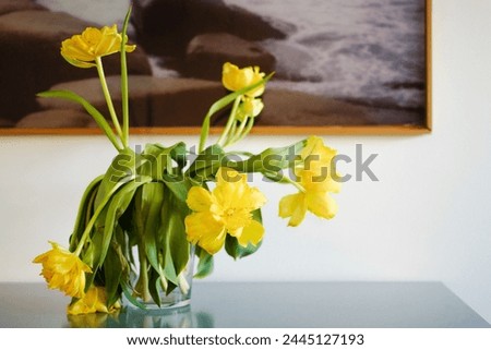 withered yellow tulips in a vase in front of a framed picture
