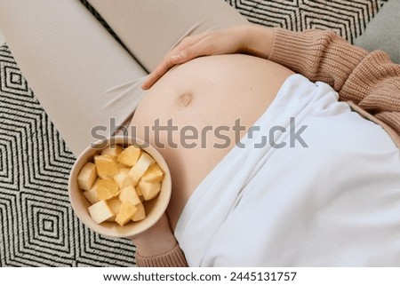 Wellness in pregnancy eating. Leisurely maternity meal. Love for healthy eating. Top view of unknown pregnant woman with bare belly holding bowl with fruits and touching her tummy Royalty-Free Stock Photo #2445131757