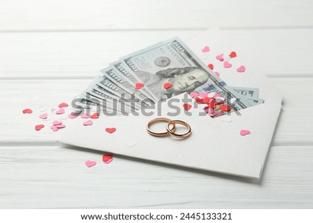 Honeymoon concept. Two golden rings, money and cutout hearts on white wooden table