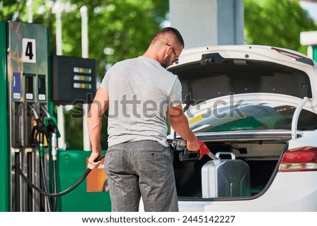 Young man refueling canister with fuel. Skilled driver filling cistern with gasoline in case of unforeseen circumstances. Male adult with pump nozzle refueling canister in car trunk. Royalty-Free Stock Photo #2445142227