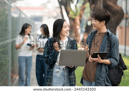 Asian college student focusing on laptop work or reading while other classmates in the background, outdoor portrait on campus campus.