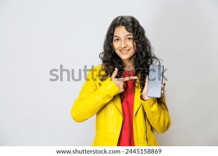 Pakistani Girl, Surprised and excited. Showing her phone's blank screen. Feeling very happy, shows from her expressions. Wearing a funky leather yellow jacket