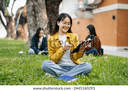 Asian Students are studying the campus park. Young people are spending time together. Reading book, working with laptop and tablet sitting on green park