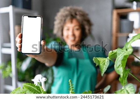 Mature smiling woman gardener showing a mobile phone screen towards camera. Mobile phone apps for home gardening