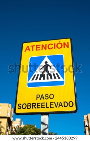 Low angle view of Spanish pedestrian zebra crossing road sign, against a clear blue sky.