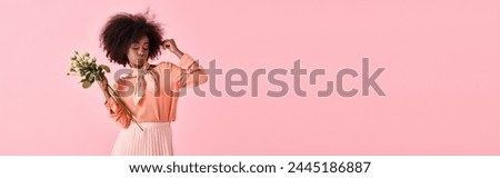 african american girl in peach fuzz attire holding flowers and looking down on pink backdrop, banner