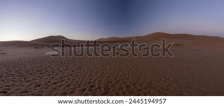 Panoramic picture of the red dunes of the Namib Desert with footprints in the sand against a blue sky in the evening light in summer